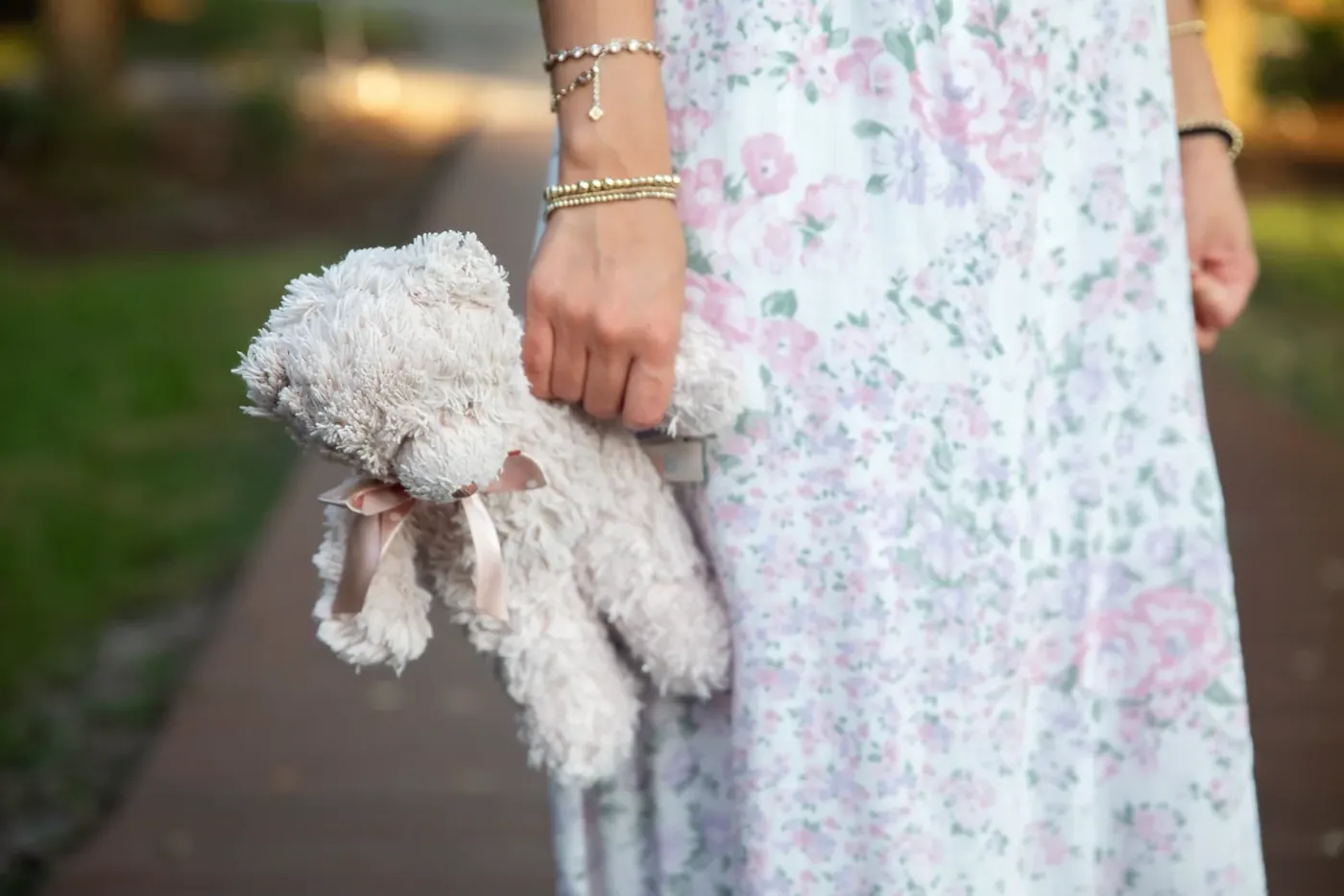 A hand with gold bracelets holding a well-loved teddy bear.